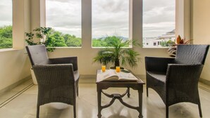 Un balcón con sillones de mimbre, una mesa con un libro y dos vasos de jugo de naranja, y una planta en maceta.
