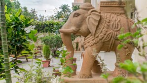 Una estatua grande de un elefante en un jardín al aire libre, con plantas en macetas y un banco de madera.