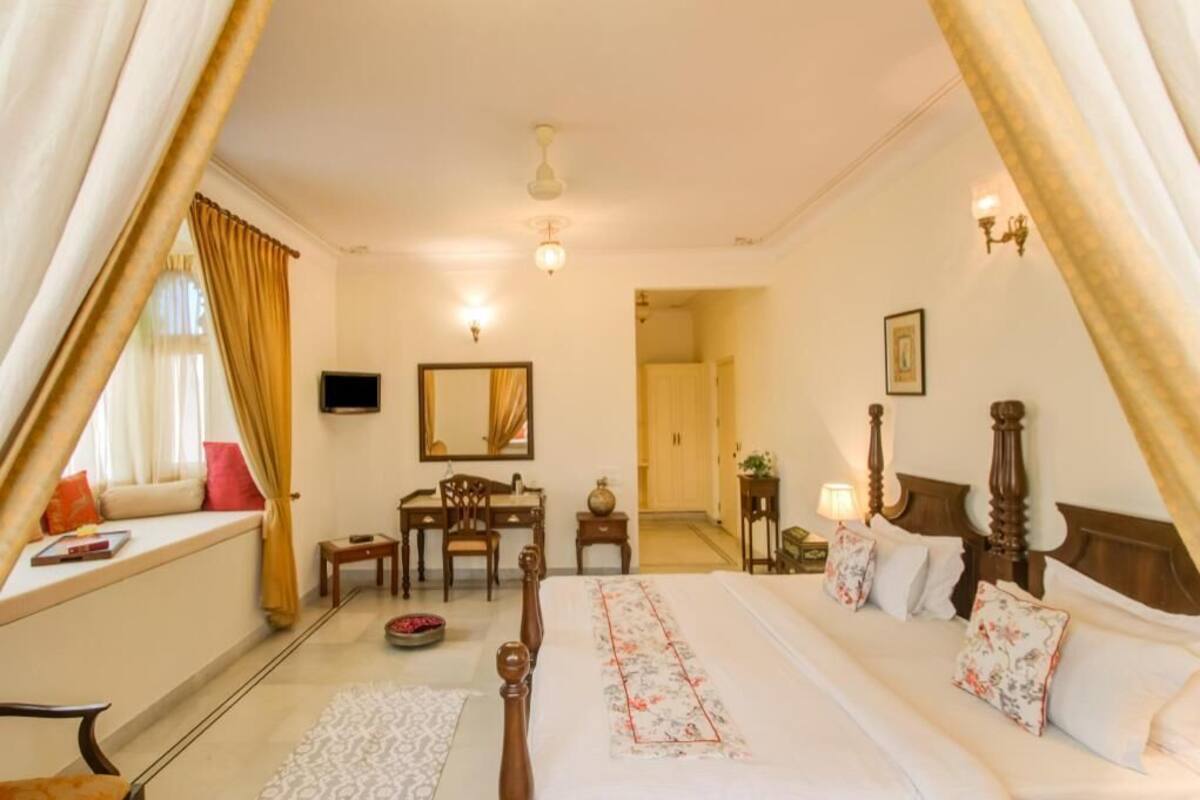 Ein Schlafzimmer mit Bett, Nachttischen, Schreibtisch, Stuhl, Spiegel und Vorhängen.