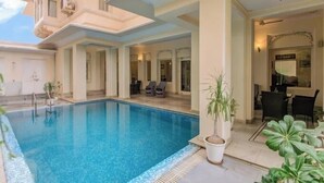 Un área de piscina con una piscina azul cristalina, sillas de descanso y un comedor con mesas y sillas.