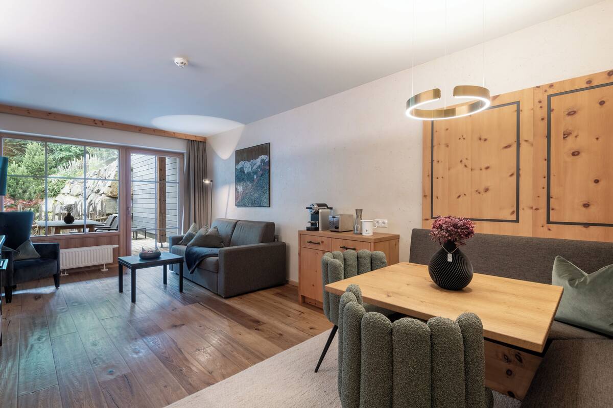 Una sala moderna con una mesa de comedor de madera, sillas tapizadas en gris, un sofá gris y un mueble de madera.