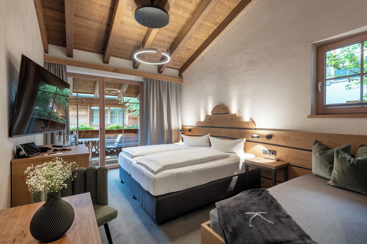 Una habitación de hotel moderna con techo de madera, una cama grande, una mesita de noche, un televisor y una ventana con vistas a zonas verdes.