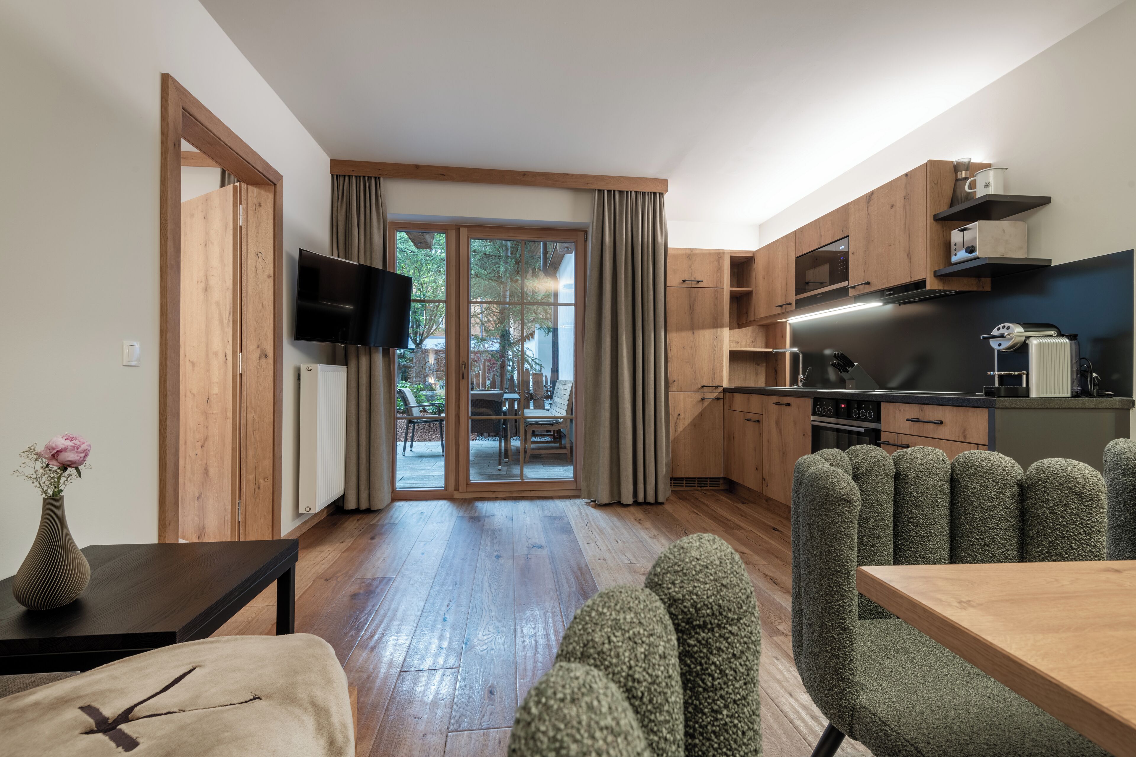 Une cuisine moderne avec des armoires en bois, un four encastré et un four à micro-ondes. On y trouve un coin repas avec une table et des chaises, ainsi qu’un téléviseur fixé au mur.