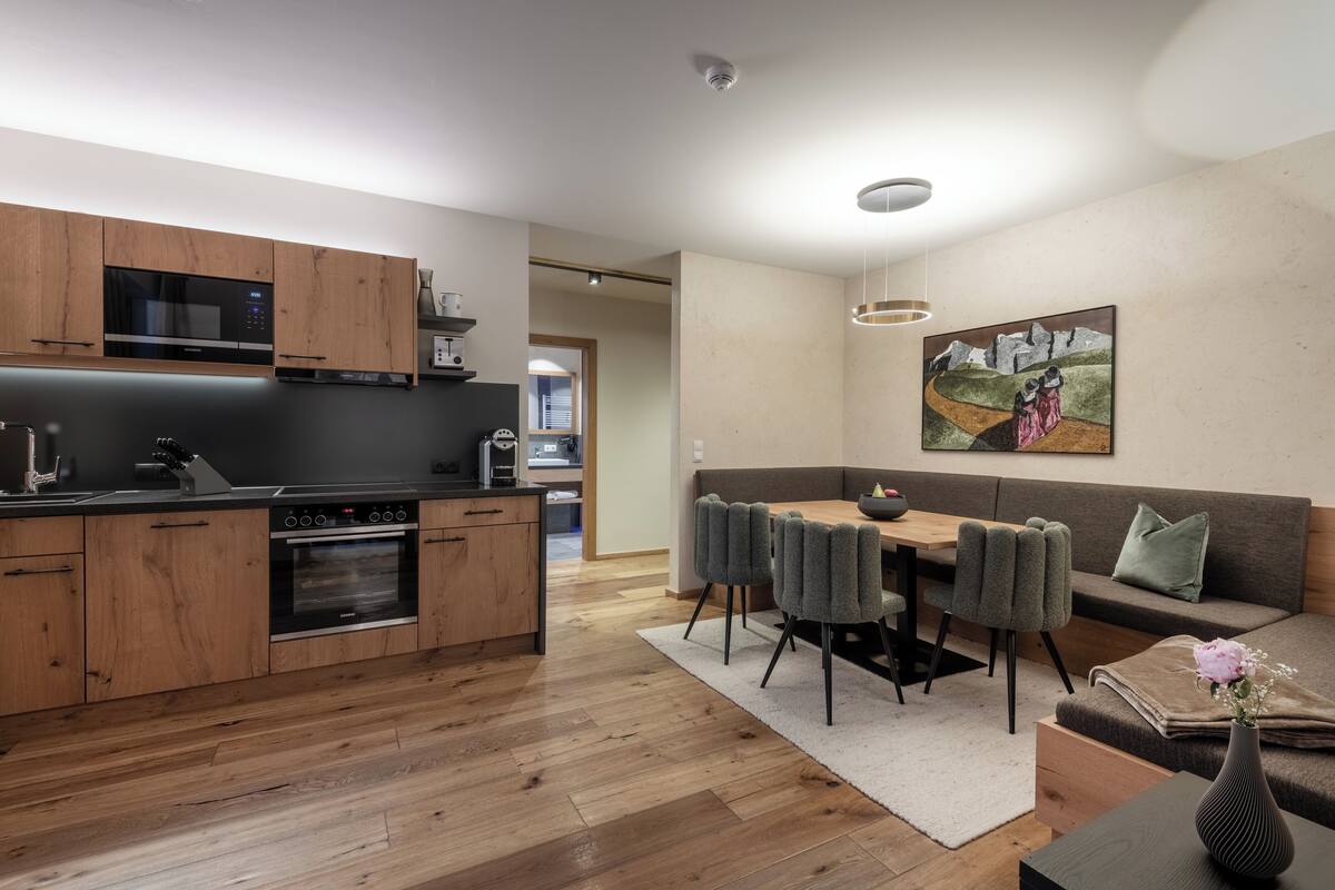 Una cocina moderna con armarios de madera y electrodomésticos de acero inoxidable, un comedor con mesa y sillas, y una sala de estar con sofá y un cuadro en la pared.