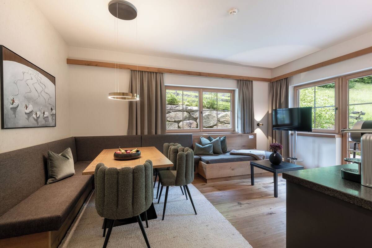 Una sala de estar moderna con una mesa de comedor de madera, sillas tapizadas en gris, un sofá gris y una pared de piedra.
