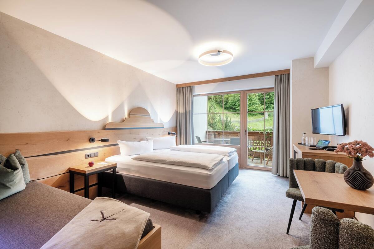 Una habitación de hotel moderna con una cama grande, un escritorio, un televisor y vistas al exterior.