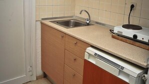 A compact kitchen with a sink, wooden cabinets, and a built-in dishwasher. - Kapsohora Inn Hotel (Kassandra)