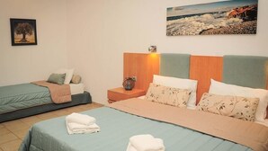A hotel room with two beds, a nightstand, and a painting of a beach scene. - Kapsohora Inn Hotel (Kassandra)