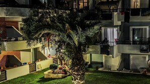 A multi-story residential building with balconies, a well-maintained lawn, and a central palm tree. - Kapsohora Inn Hotel (Kassandra)