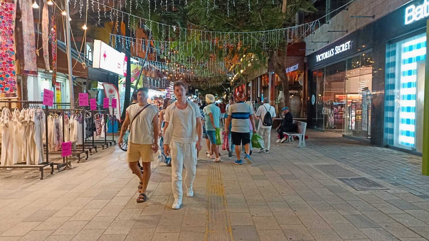 A busy pedestrian walkway with shops and hanging lights.