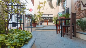 Un patio con suelo de baldosas hexagonales, plantas en macetas, una mesa de madera y un edificio con el cartel de un centro médico.