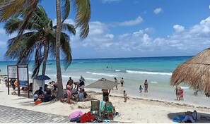 A beach with palm trees, a thatched umbrella, and people relaxing. - Beach House Hotel (Playa del Carmen)