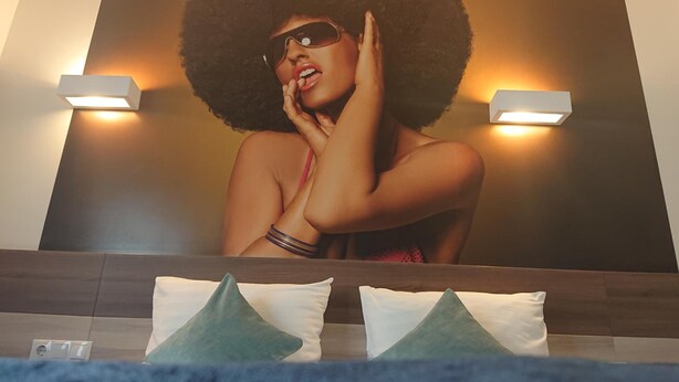 A hotel room with a large mirror, two wall-mounted lights, and a bed with pillows. - Algiro Hotel (Kaunas)