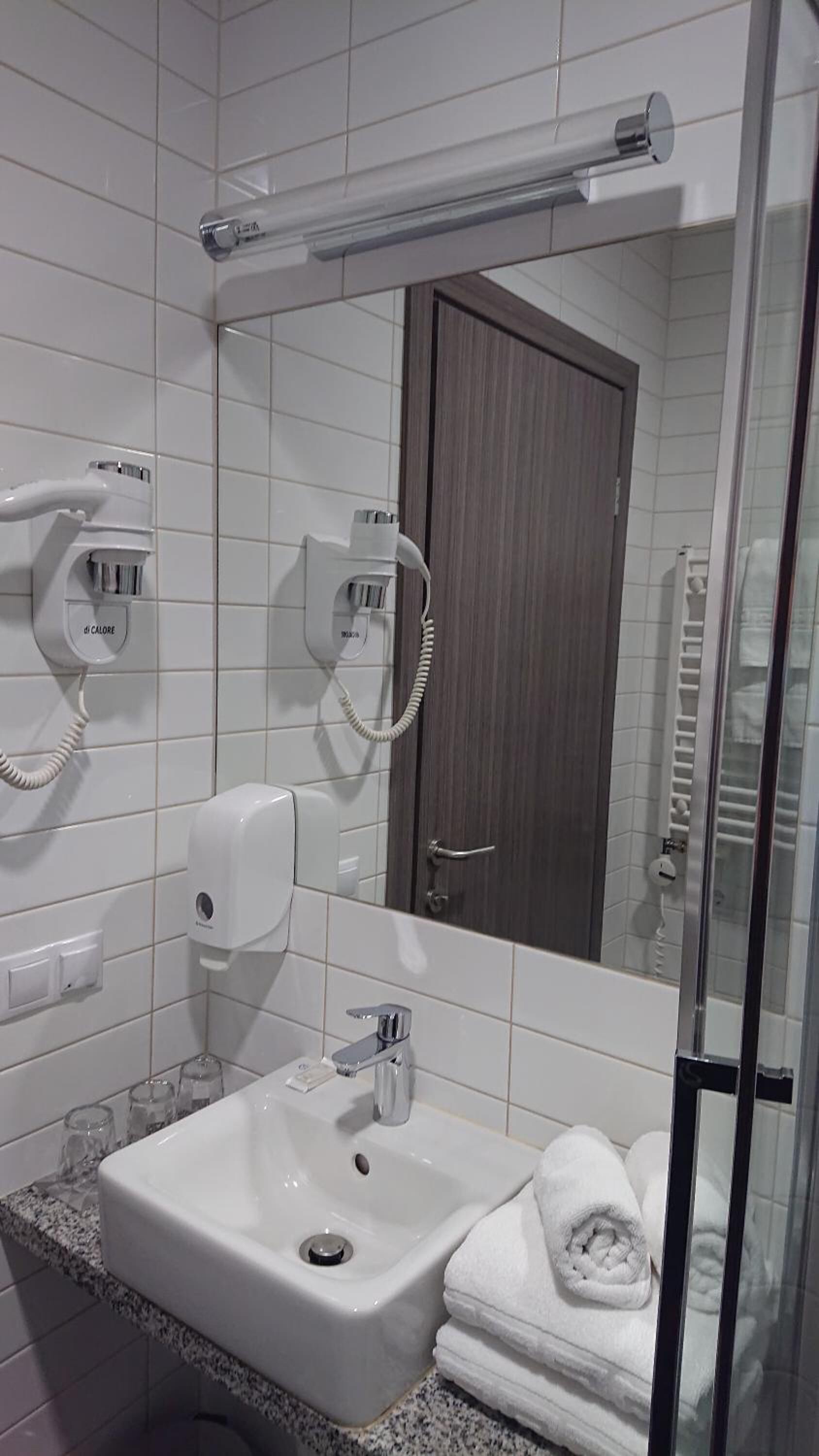 Une salle de bain équipée d’un lavabo, d’un porte-serviettes et de deux sèche-cheveux fixés au mur.