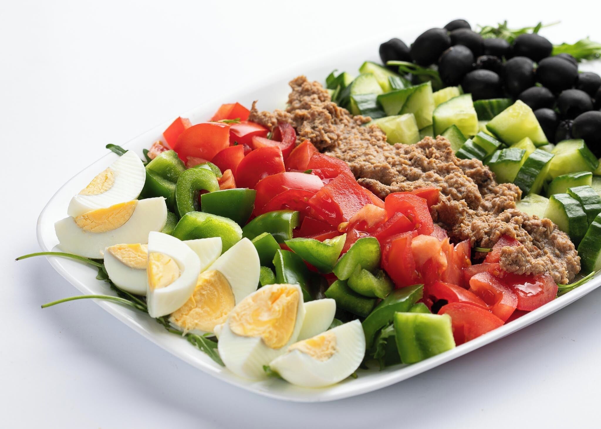 A plate of food with sliced cucumbers, tomatoes, green peppers, black olives, and a meat-based dish.