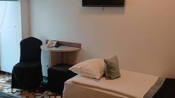 Ein Hotelzimmer mit Bett, Schreibtisch mit Telefon, Stuhl, Wandfernseher und einem gemusterten Teppich.