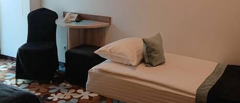 A hotel room with a bed, a desk with a telephone, a chair, a television mounted on the wall, and a patterned carpet.