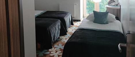 Habitación de hotel con dos camas, un radiador, una ventana con cortinas, una puerta y un cartel de no fumar.