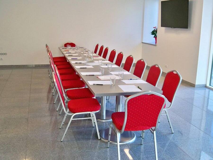 Een vergaderzaal met een lange tafel, rode stoelen en een televisie aan de muur.