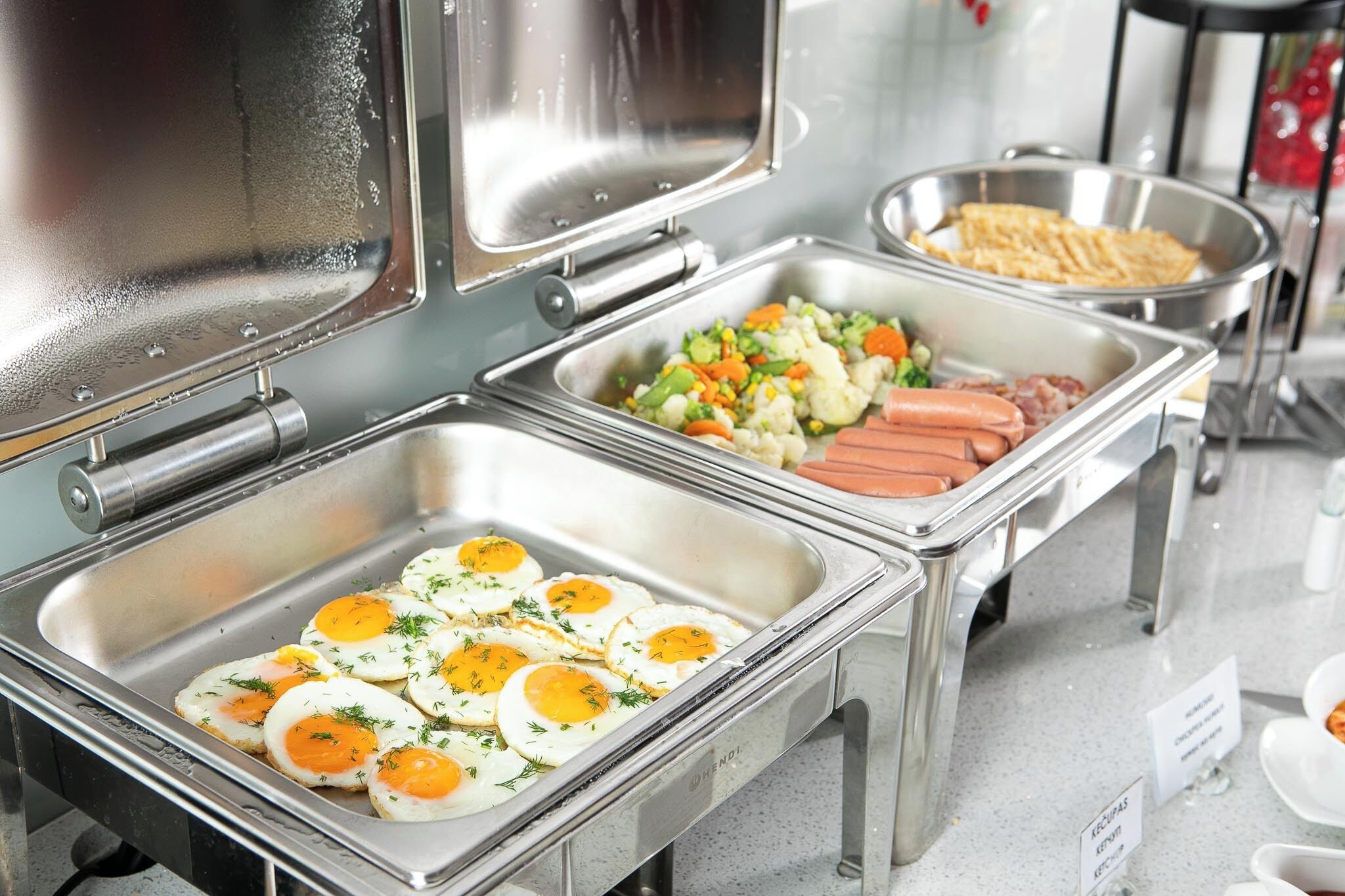Un buffet proposant une variété de plats, notamment des œufs, des légumes et des saucisses.