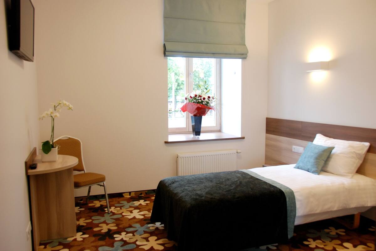 Ein Schlafzimmer mit Bett, Sessel, kleinem Tisch, Fenster mit Blick und Heizkörper.