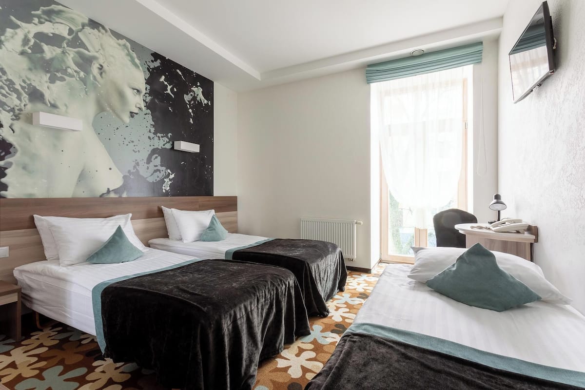 Ein Hotelzimmer mit zwei Betten, einem großen abstrakten Gemälde an der Wand, einem Heizkörper, einem Schreibtisch mit Telefon und einem Sessel.