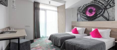 A hotel room with two beds, a desk, and a large window.