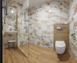 Un baño moderno con salpicadero de mármol, tocador de madera, lavabo, inodoro y cabina de ducha con mampara de cristal.
