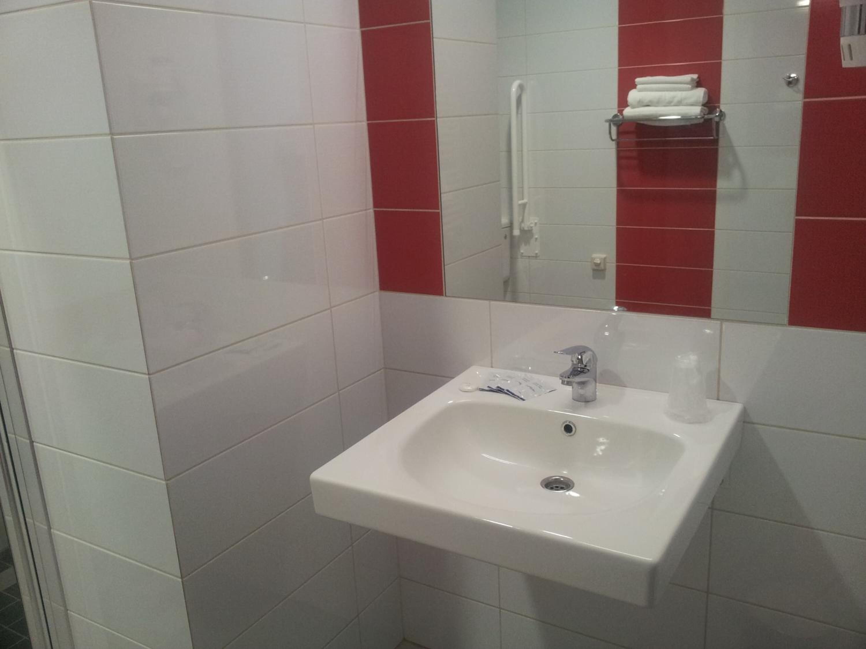 Un baño con un lavamanos blanco, un espejo y paredes de baldosas rojas.