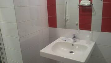 Un baño con un lavamanos blanco, un espejo y paredes de baldosas rojas.