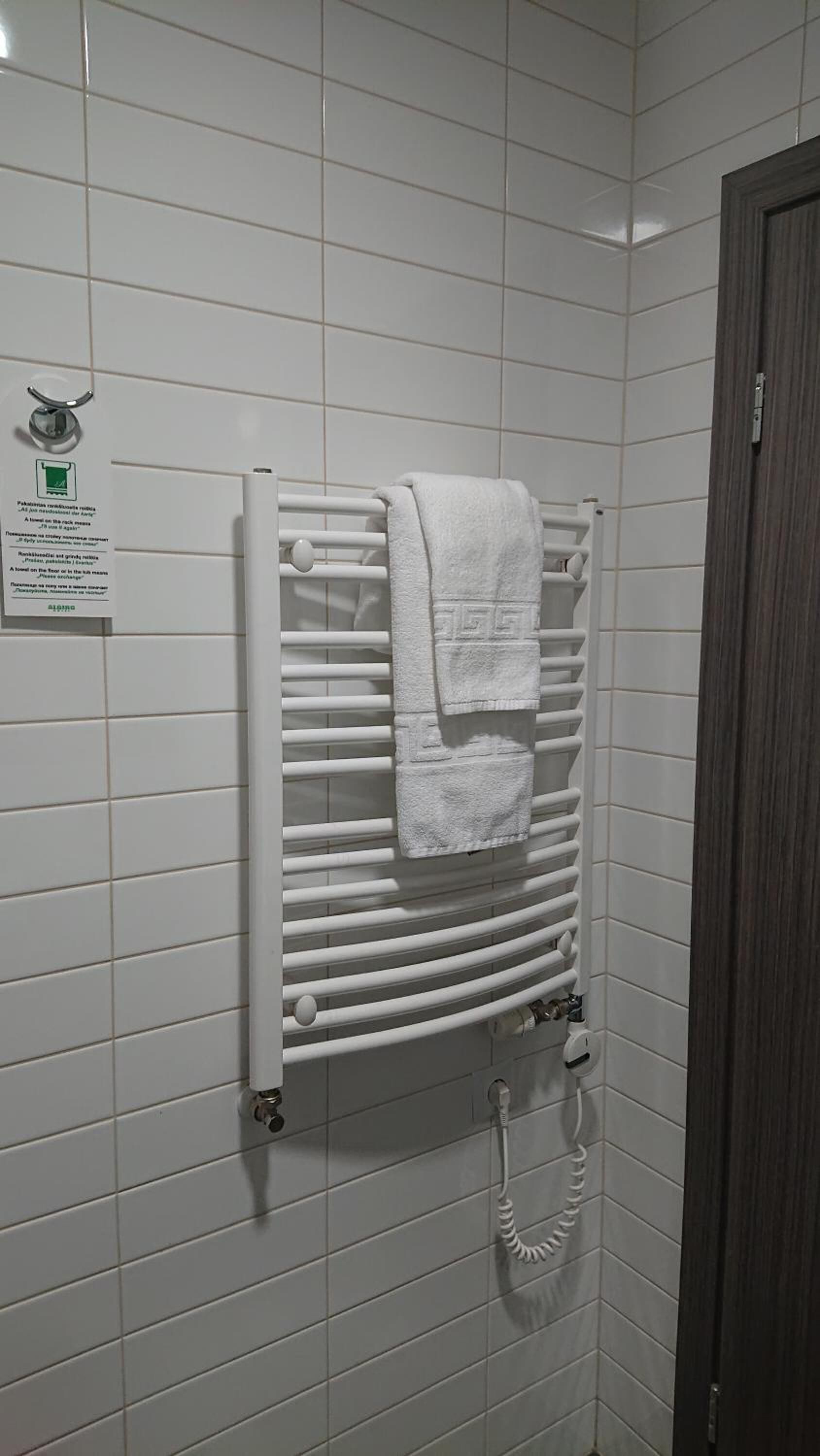 A bathroom with a white towel rack holding two towels, a sign with text, and a shower area.