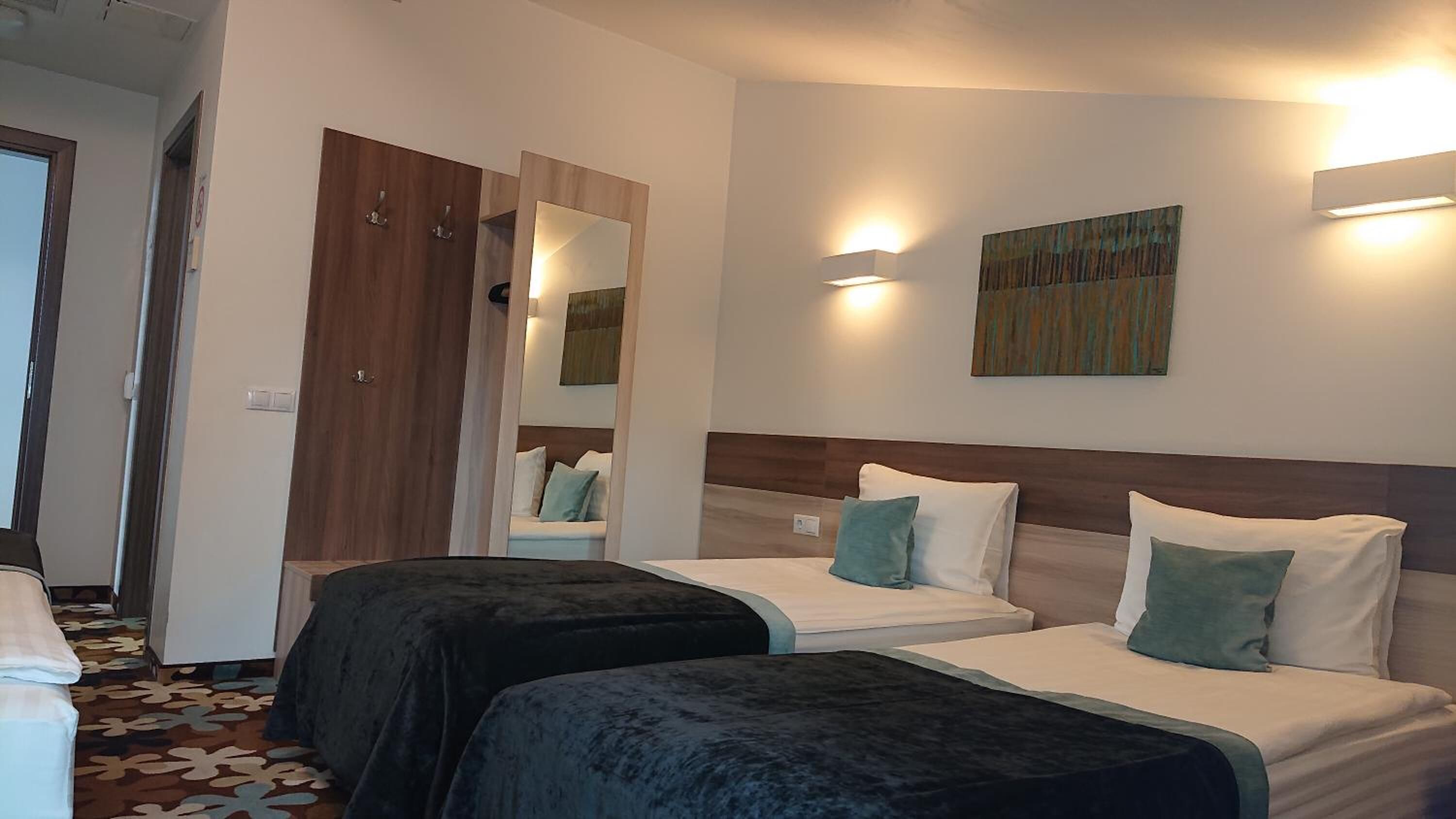 Una habitación de hotel con dos camas, un armario de madera, un espejo y un cuadro en la pared.