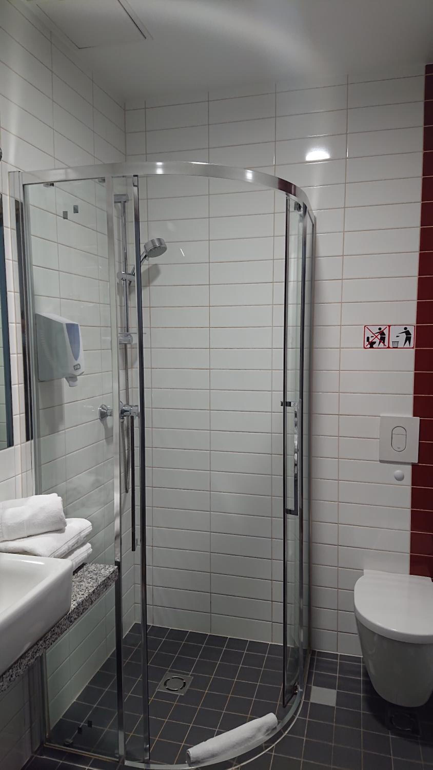 Un baño moderno con ducha envuelta en vidrio, paredes de azulejos blancos, un lavamanos blanco con encimera de mármol y un inodoro blanco.