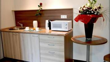 Una cocina compacta con microondas, lavamanos y una pequeña mesa con un florero.