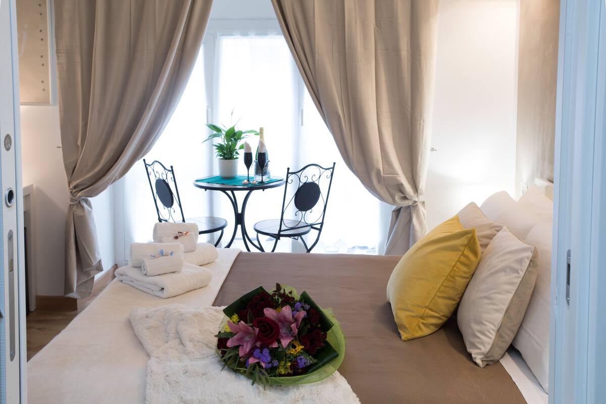 A hotel room with a bed, a table with a plant, and a window with curtains.