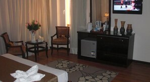 A hotel room with a bed, two chairs, a small table with a vase, a television, and a fireplace. - Cairo plaza Guest House (Sheikh Zayed City)