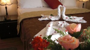 A neatly made bed with white towels arranged in a heart shape, a red pillow, and a bouquet of flowers on the bedside table. - Cairo plaza Guest House (Sheikh Zayed City)
