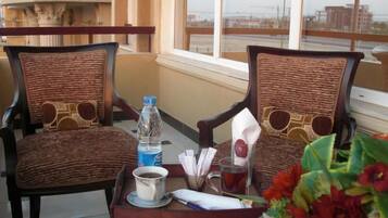 Two wicker chairs with circular cutouts, a tray with a water bottle, a cup of coffee, a glass of tea, and a napkin.