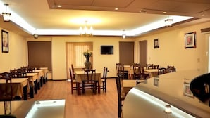 A dining area with multiple tables and chairs, a central table with a vase of flowers, and a television on the wall. - Cairo plaza Guest House (Sheikh Zayed City)
