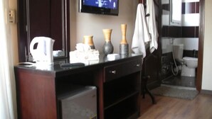 A hotel room with a wooden desk, a flat-screen TV mounted on the wall, a small seating area with a chair, and a bathroom visible in the background. - Cairo plaza Guest House (Sheikh Zayed City)