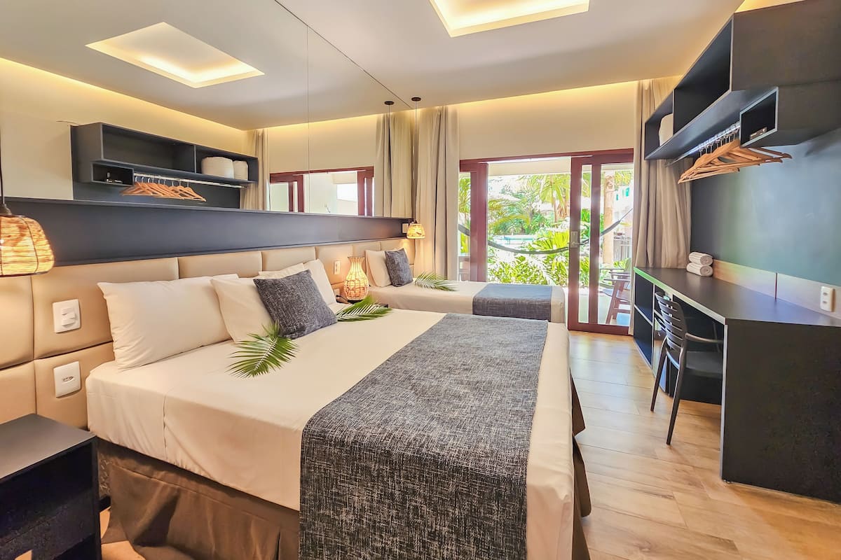 Habitación de hotel moderna con una cama grande, un escritorio y un balcón con vistas a zonas verdes.