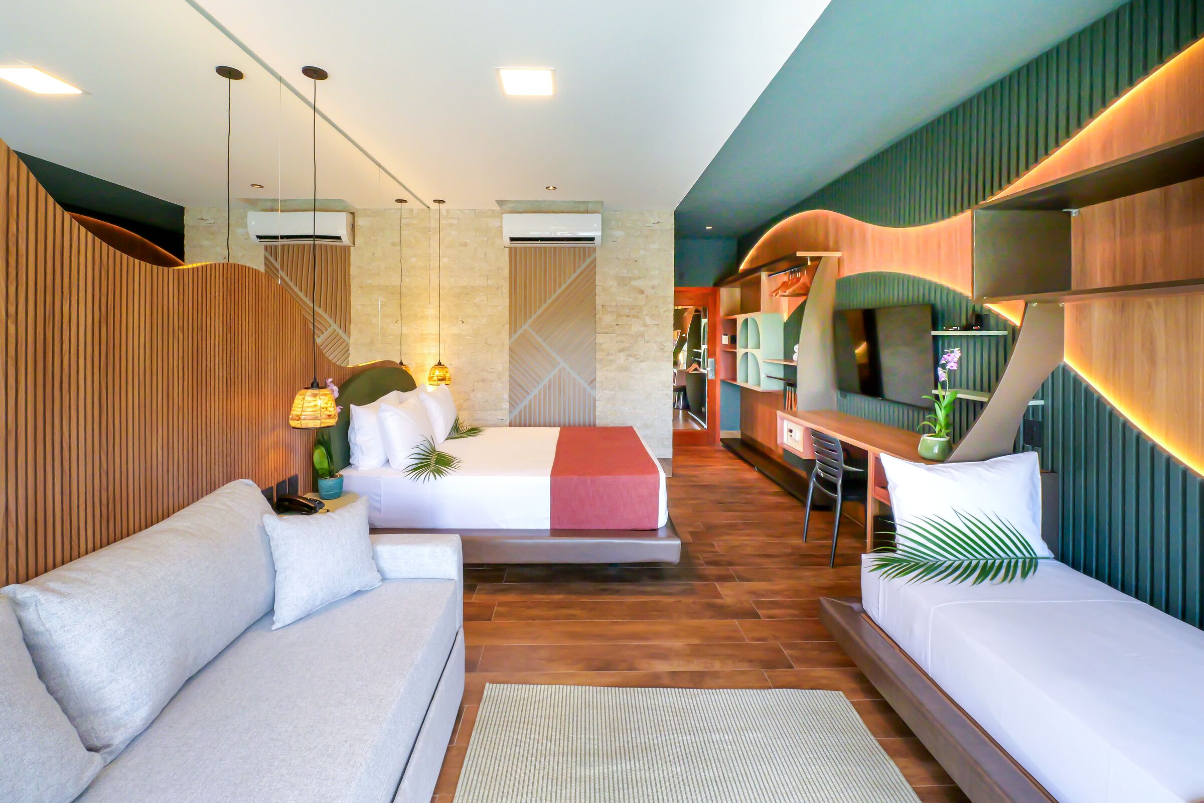 A modern hotel room with a sofa, a bed, a desk, and a TV.