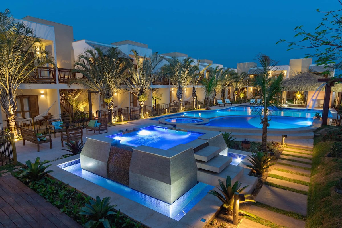 Un resort con varias piscinas, zonas de estar al aire libre y palmeras.