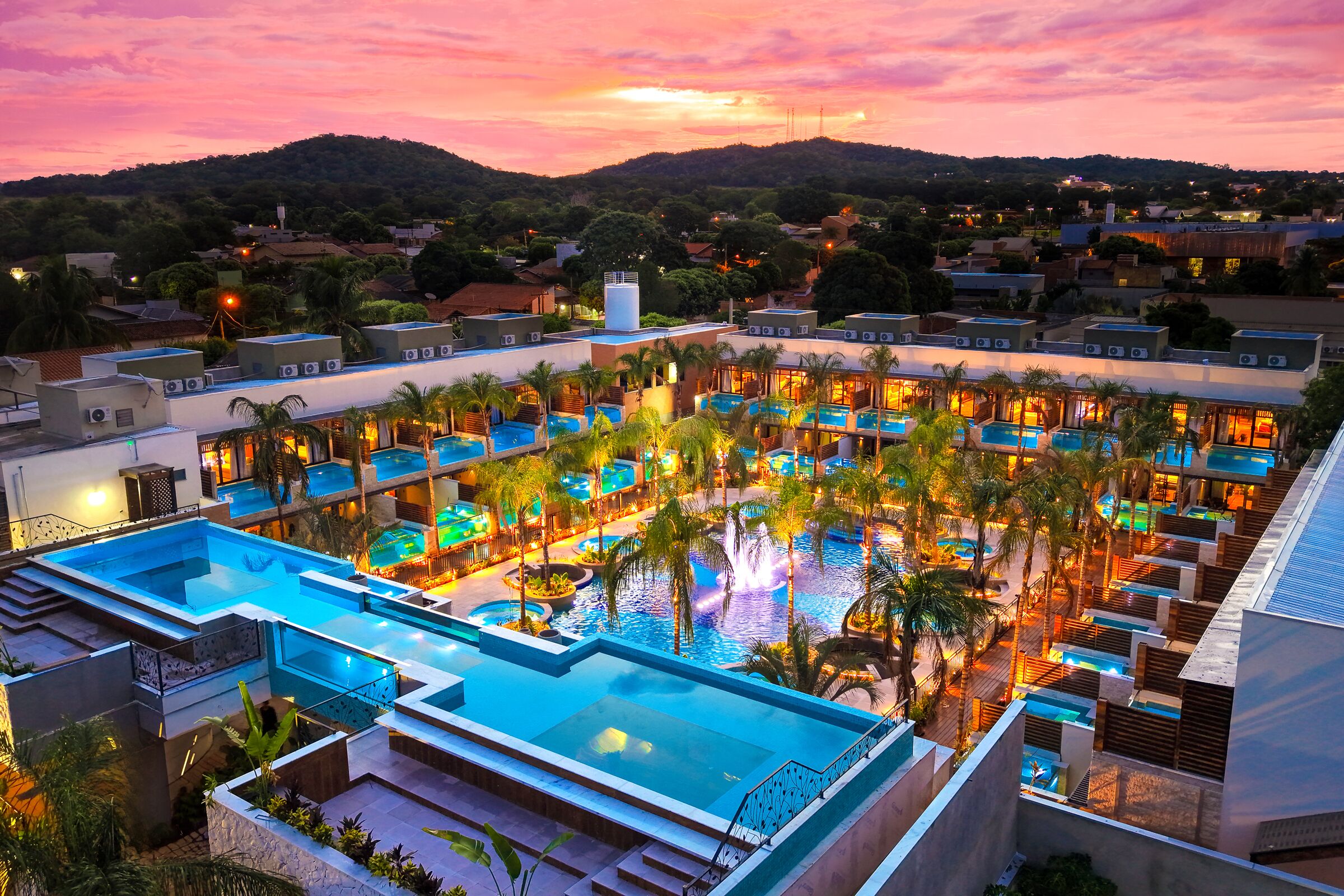 Um resort com várias piscinas, palmeiras e vista para o pôr do sol.