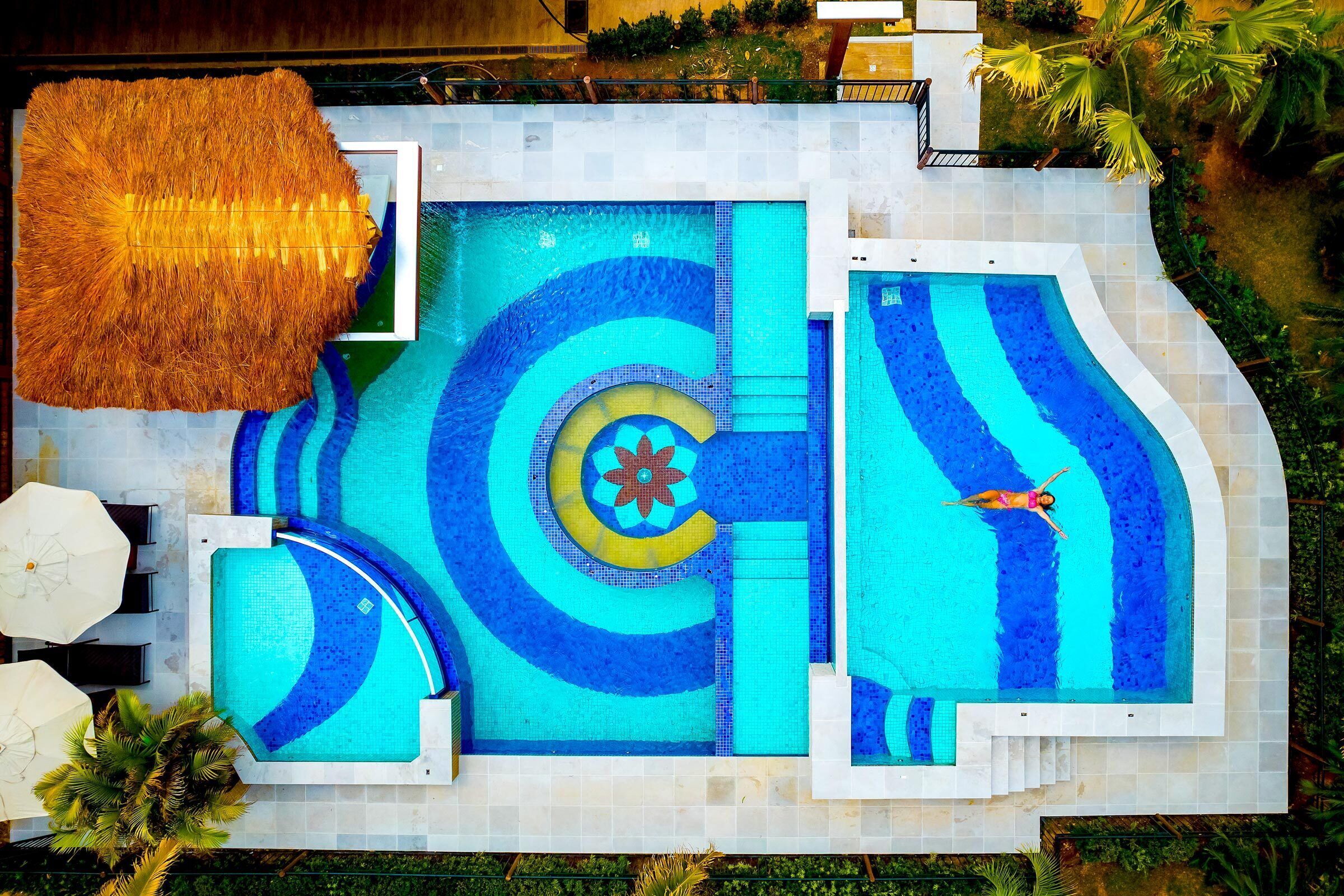 A large outdoor swimming pool with multiple sections, including a central area with a decorative pattern and a separate section with a person swimming.