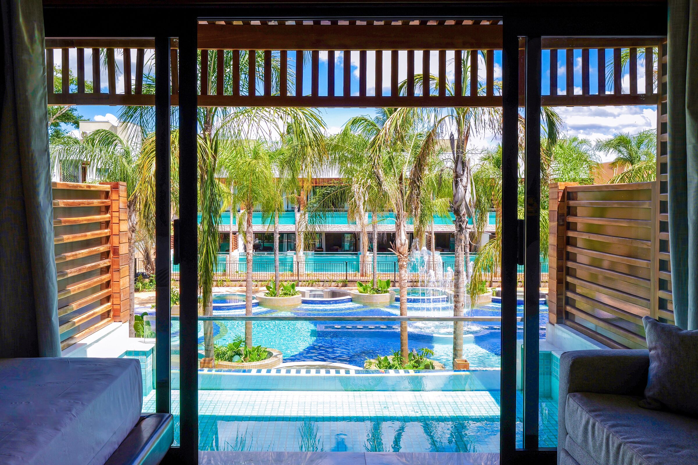A hotel room with a view of a pool area, including multiple pools and palm trees.