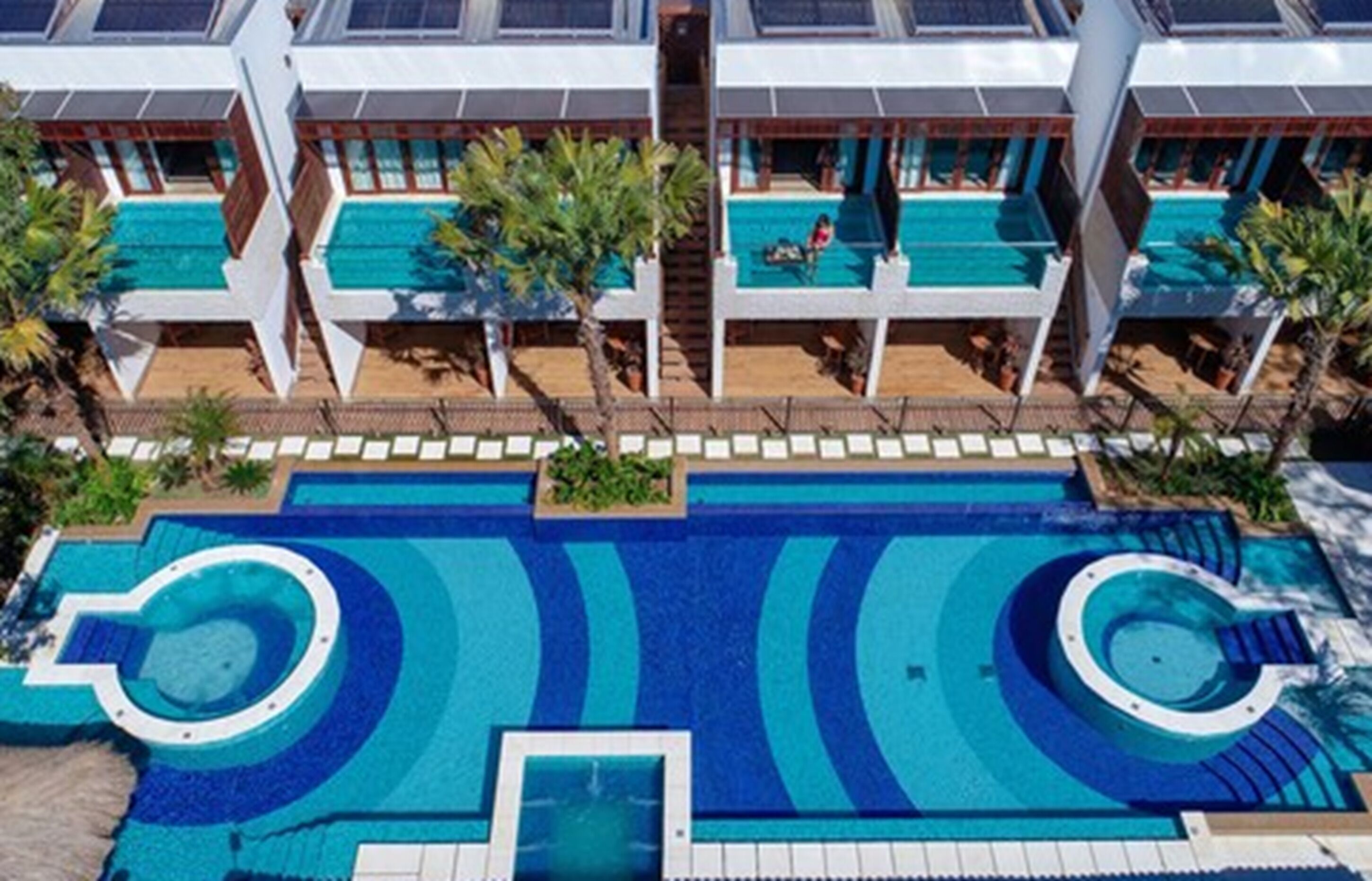 Un hotel moderno con varias piscinas, incluyendo una piscina central grande y piscinas más pequeñas conectadas por senderos.