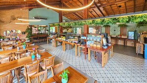 Un restaurant spacieux avec des tables et des chaises en bois, un plafond haut avec des poutres apparentes, et une variété de plantes et de verdure.