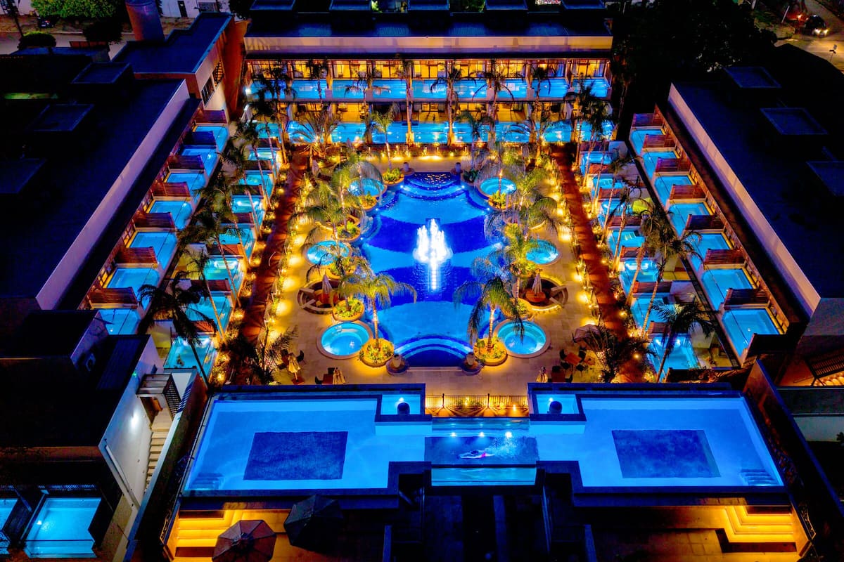 Un hotel con múltiples piscinas, una fuente central y un área exterior bien iluminada.