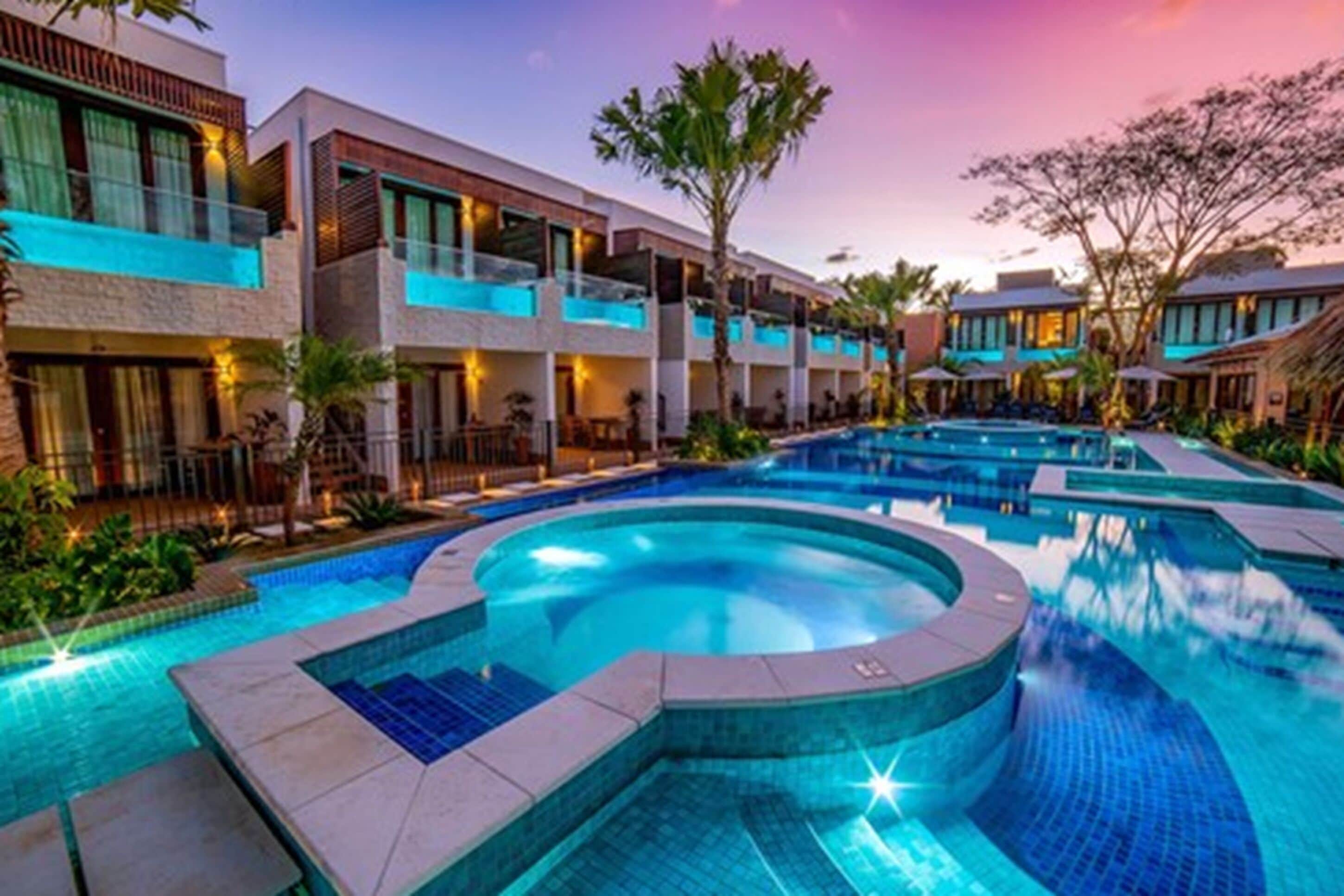 Resort com uma grande piscina central, várias varandas e paisagismo exuberante.